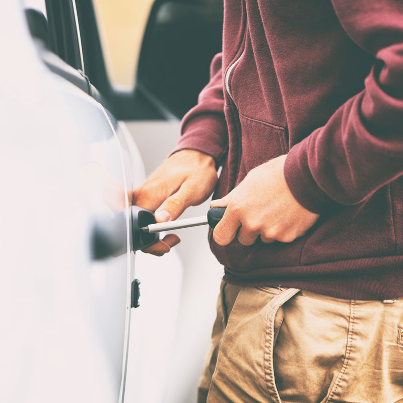 Close-up of a man trying to break into a car with a screwdriver