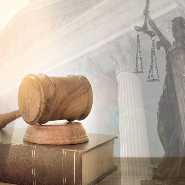 Gavel on top of law book with a statue of Lady Justice and a courthouse in the background