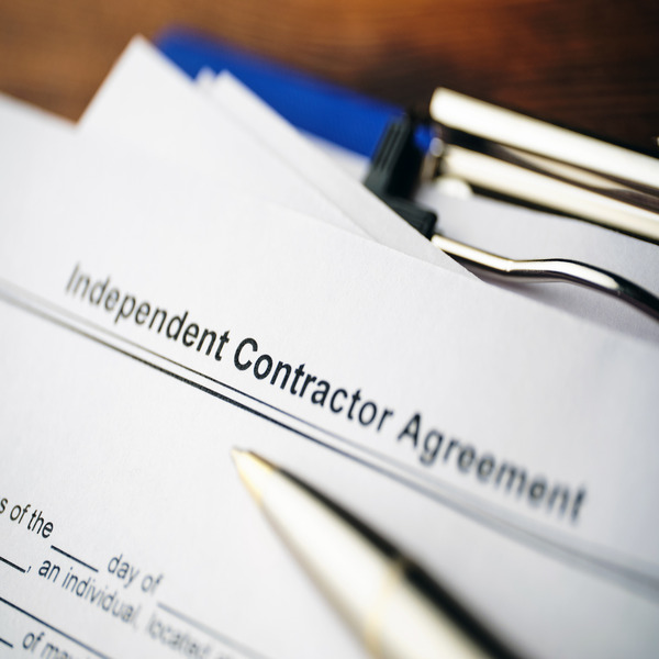 Close-up of an independent contractor agreement, blue clipboard, and silver pen