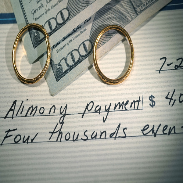 Close-up of alimony check with cash and gold wedding rings